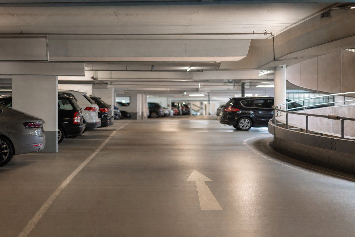 Innenansicht einer modernen Parkgarage mit parkenden Autos, Betonpfeilern und einem Richtungspfeil auf der Fahrbahn